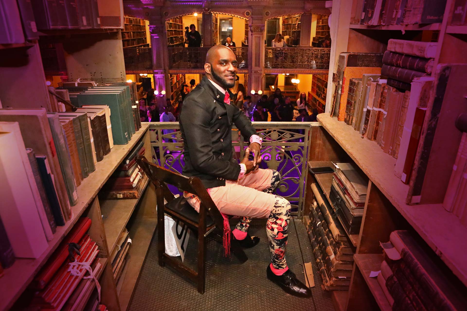A person dressed in a black vest sits in between stacks of books